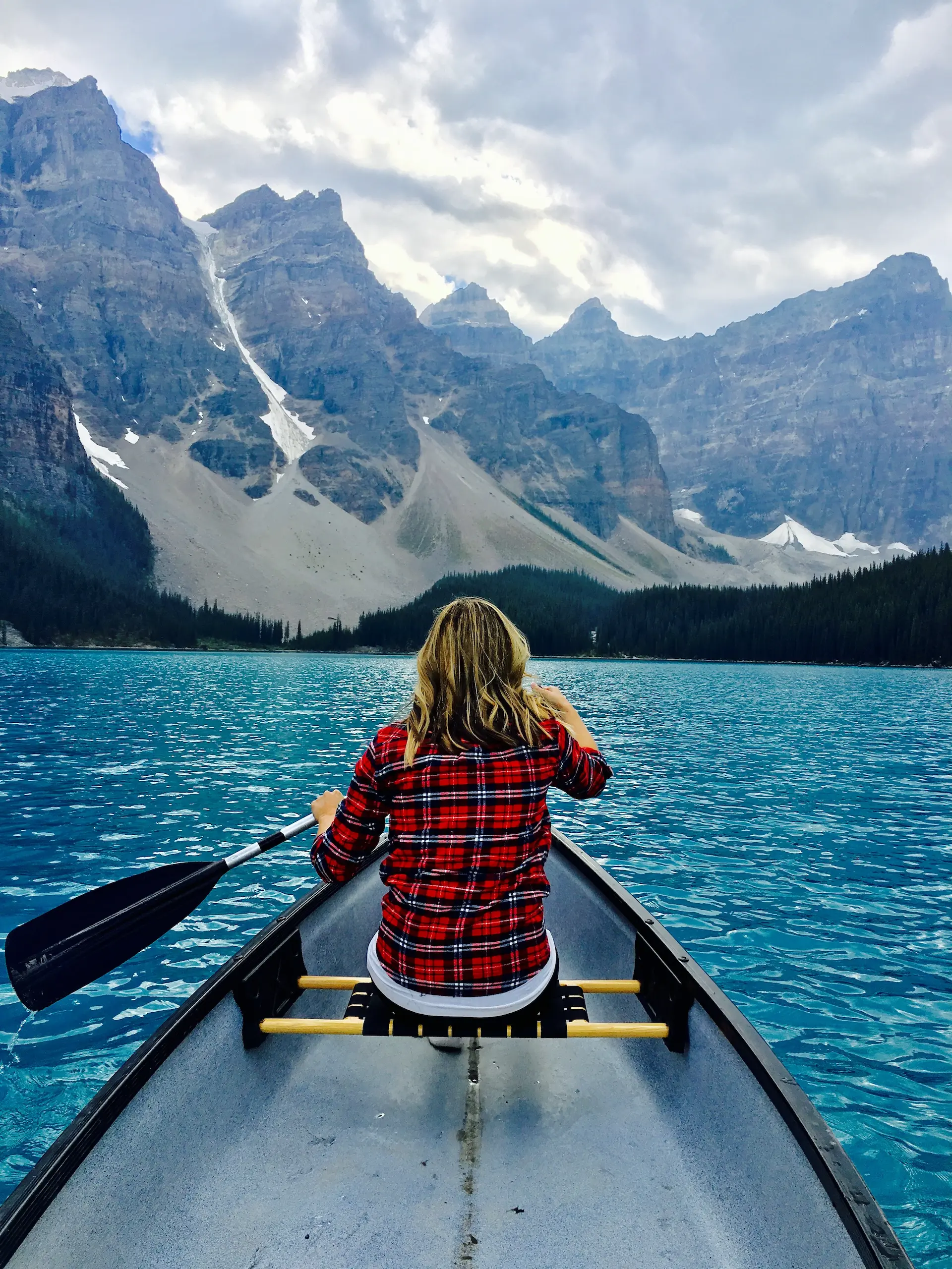 woman canoeing on a lake surrounded by high snowy mountains